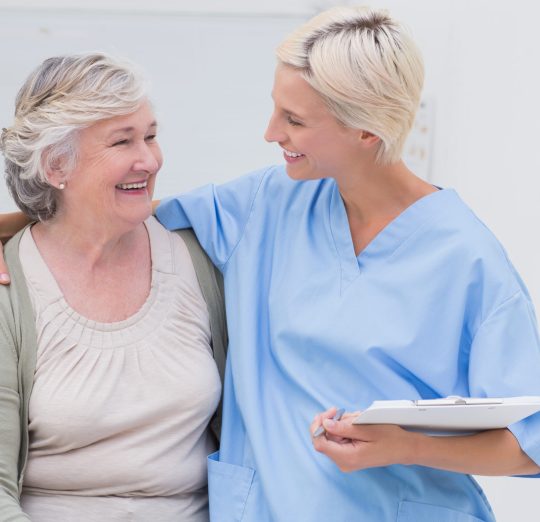 Happy friendly nurse with arm around senior patient standing in clinic